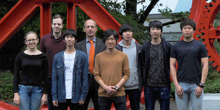 Acht Personen stehen nebeneinader vor einem roten Zahnrad auf dem Campus der Tu Dortmund