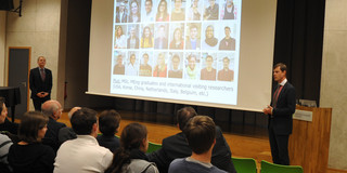 BCI Jubilee Lecture mit Marc-Olivier Coppens Redner steht neben einem Rednerpult, eine Beamerwand zeigt eine Präsentation, Zuschauer sitzen im Publikum
