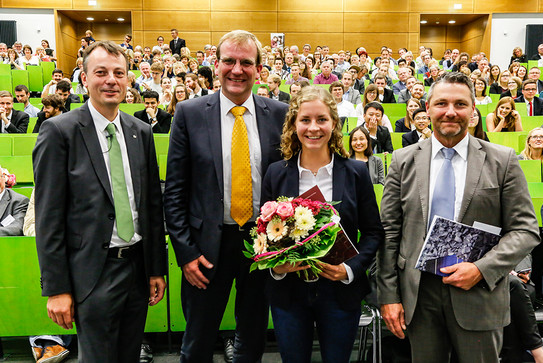 Drei Männer und eine Frau stehen im Hörsaal vor Publikum