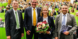 Drei Männer und eine Frau stehen im Hörsaal vor Publikum