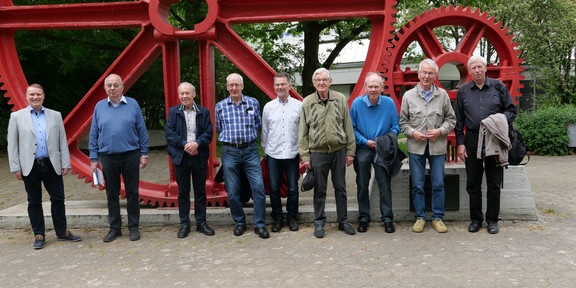 Gruppenfoto von Ehemaligen vor roten Zahnrädern