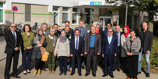 Eine Gruppe von Frauen und Männern stehen draussen vor einem Gebäude in zwei Reihen nebeneinander