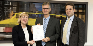 Dr. Stefan Krämer zum Honorarprofessor ernannt Eine Frau und zwei Männser stehen nebeneinander in einem Raum, im Hintergrund ein Gemälde