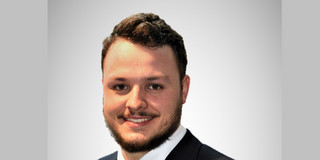 Portraitfoto von Michael-David Fischer. Er trägt einen Anzug mit farbiger Krawatte, hat dunkles, kurzes Haar und ist geschätzt Mitte 20.