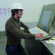 Ein Mann mit weissem Schutzhelm bedient eine Anlage am Monitor