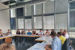 Gruppe von Personen, die in Hufeisenform an Tischen sitzen und miteinander sprechen