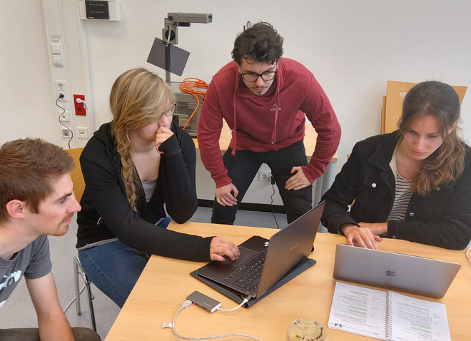 4 Studierende an einem Tisch in einer gemeinsamen Arbeitssituation auf ein Laptop schauend