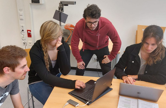 4 Studierende an einem Tisch in einer gemeinsamen Arbeitssituation auf ein Laptop schauend