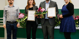 Zwei Männer und zwei Frauen stehen vor einer Tafel nebeneinander. Die Personen in der Mitte halten Urkunden und Blumensträusse in den Händen
