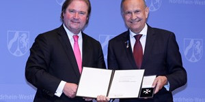 Zwei Männer stehen nebeneinander und halten eine Urkunde und einen Orden in den Händen