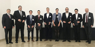 Neun Personen stehen nebeneinander in einem Raum vor einer weissen Wand