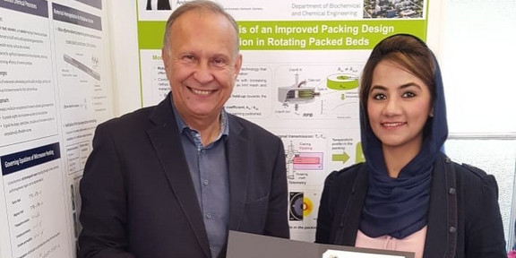 Ein Mann und eine Frau stehen vor einer Postwand. Die Frau hat eine Urkunde in der Hand