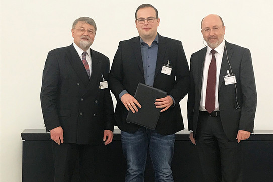 Drei Männer in Anzügen stehen nebeneinander in einem Raum