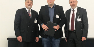 Drei Männer in Anzügen stehen nebeneinander in einem Raum