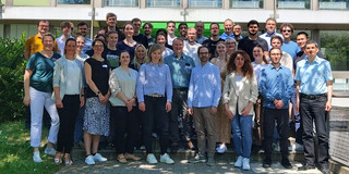 Group photo of participants at the "Teach'n tech 2025" event organized by the Department of Biological and Chemical Engineering at TU Dortmund University. The group is standing on a staircase in front of a building, surrounded by green plants. The participants are dressed in different styles of clothing and smiling at the camera.