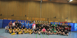 Mehrere Fußball-Teams stehen und sitzen vor einem Fußballtor in einer Sporthalle