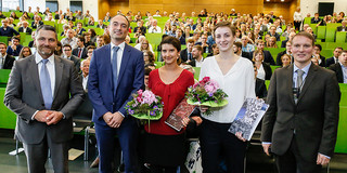 Fünf Personen stehen im Hörsaal nebeneinander, im Hintergrund Publikum.