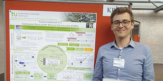 Benedikt Strakeljahn Mann steht vor einem Poster und hält eine Urkunde in der Hand