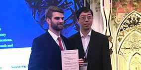 Best Poster Award der SMART 2018 an Dominik Segiet Zwei Männer stehen mit einer Auszeichnung in der Hand in einem Raum