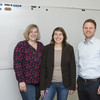 Two women and a man stand in front of a magnetic board and smile at the camera