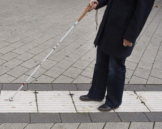 Eine blinde Person folgt dem Blindenleitsystem auf dem Campus mithilfe eines Blindenstocks